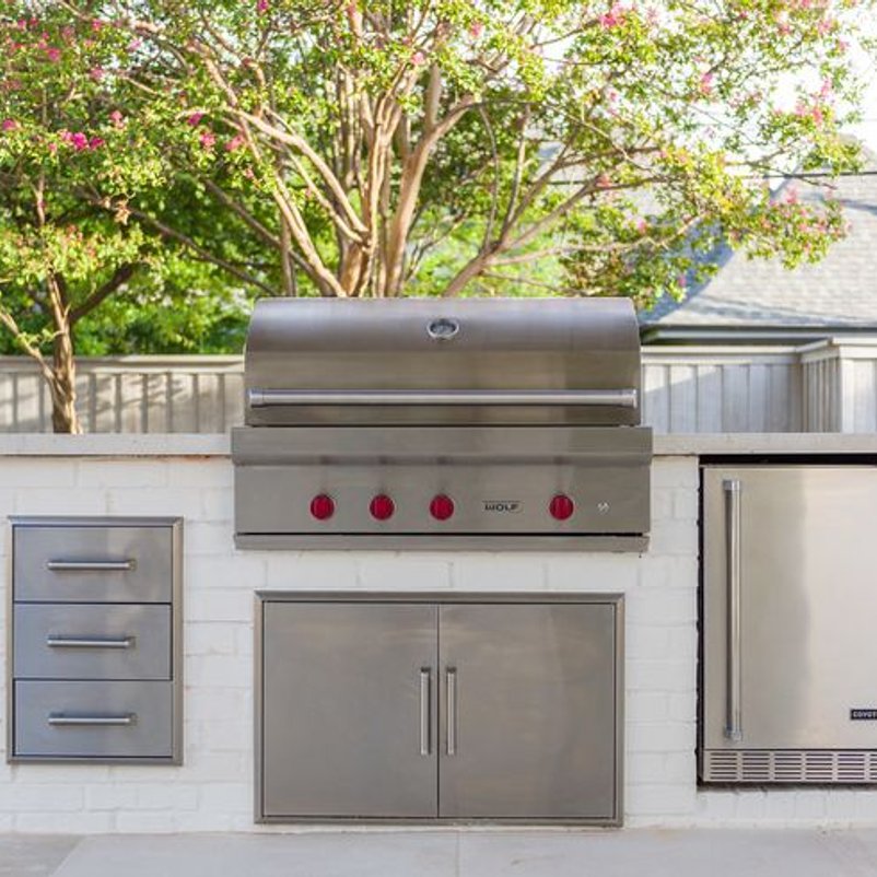 Built-in outdoor kitchen with a stone island and grill on a covered patio