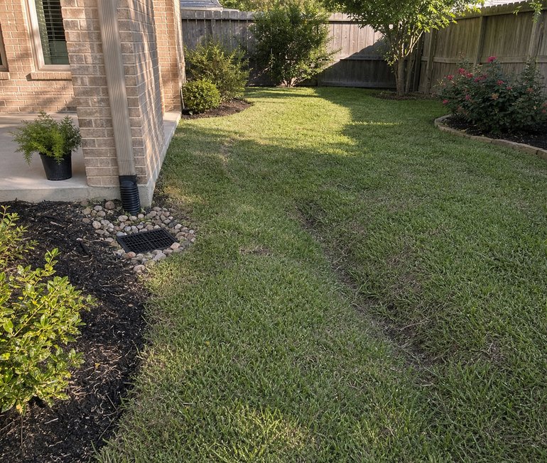 River rock yard drainage channel guiding water away from a Houston patio